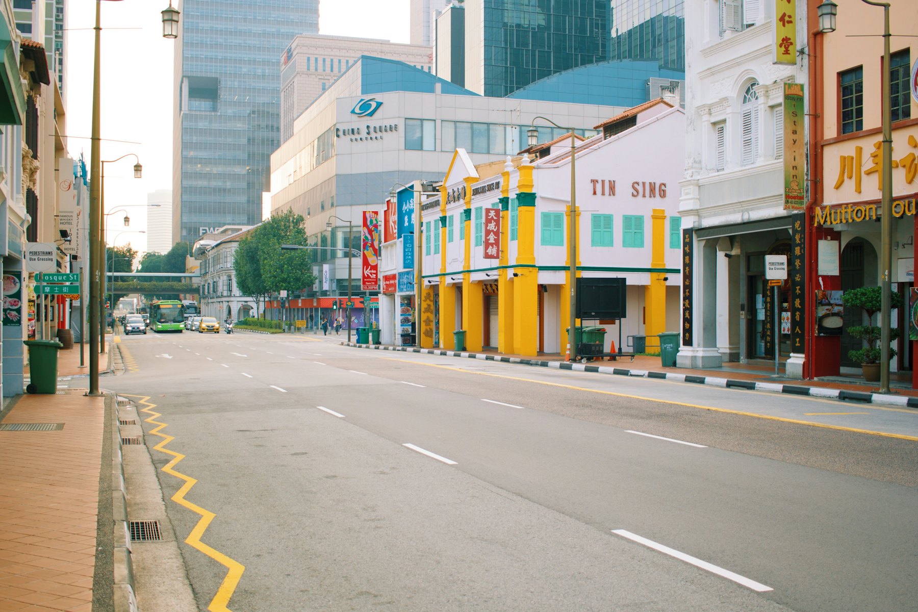 A quiet street of colourful shophouses with office towers behind, Singapore